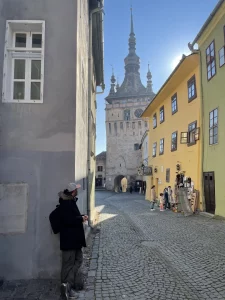 Miguel de Two On Trip explorando las calles empedradas del casco histórico de Sighisoara, la ciudad más bonita de Transilvania, con la Torre del Reloj al fondo.