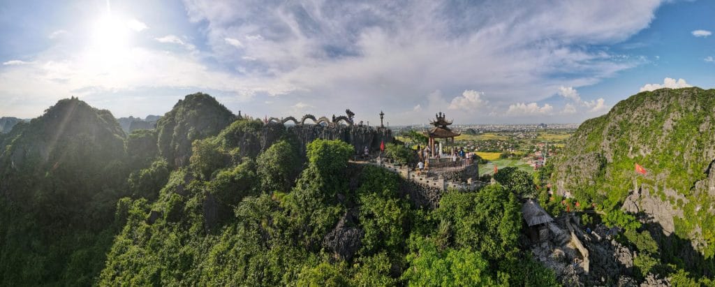 Panorámica de la montaña del Dragón en Tam Coc, Vietnam, con vistas a su famosa pagoda, un sendero de piedra con esculturas de dragones, y paisajes de vegetación y arrozales.