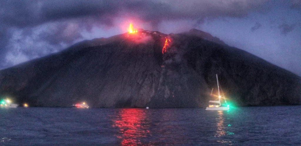 Erupción del volcán Stromboli con lava cayendo por su ladera y reflejándose en el mar.