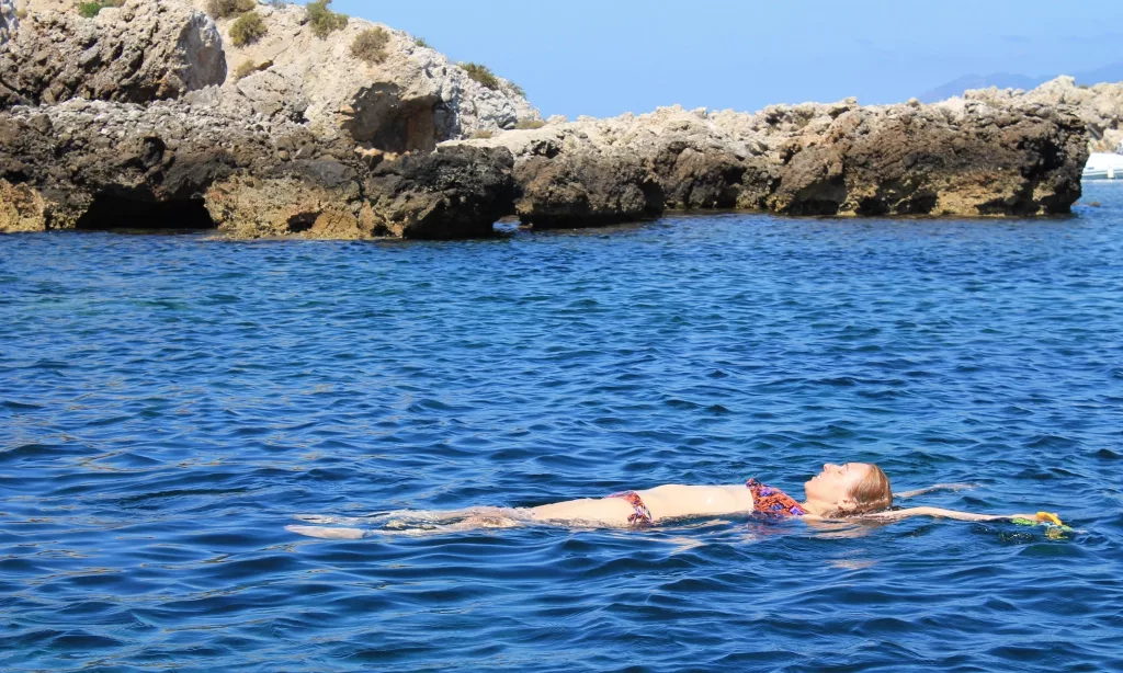 Mujer flotando en el mar cristalino de Favignana con formaciones rocosas al fondo.