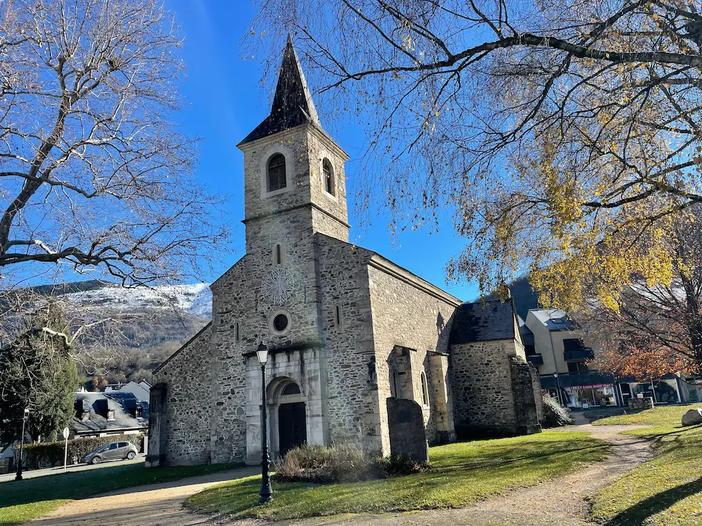 Iglesia de piedra en Saint-Lary, Pirineo Francés, con montañas nevadas al fondo

