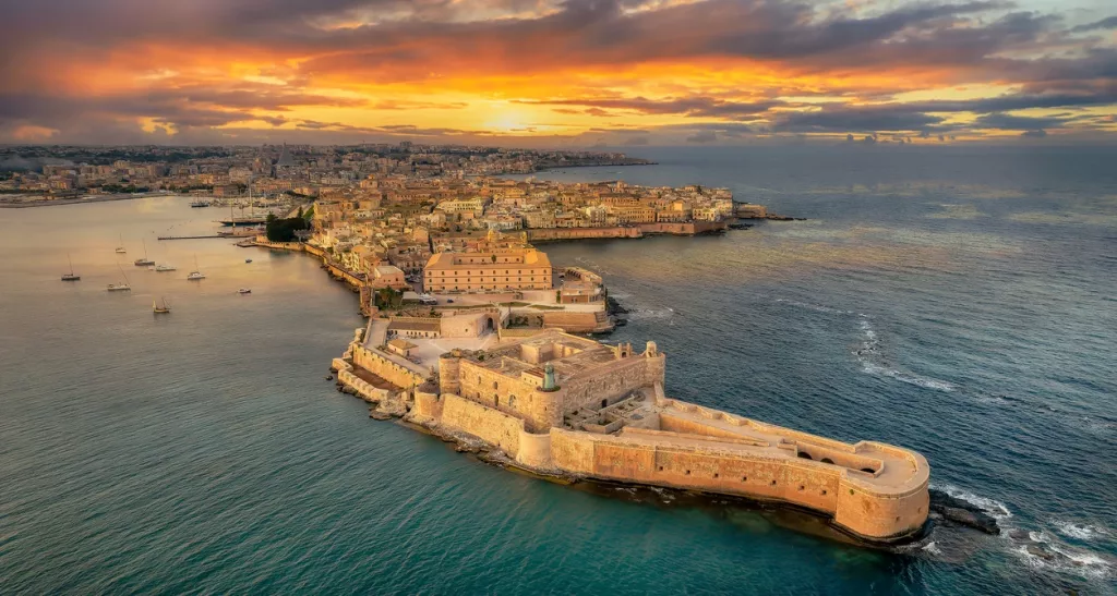 Vista aérea de la fortaleza de Ortigia al atardecer, rodeada por el mar en Siracusa.