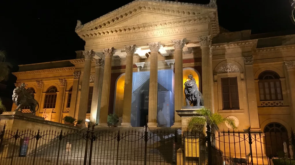 Teatro Massimo iluminado por la noche con sus icónicas esculturas de leones en la entrada.