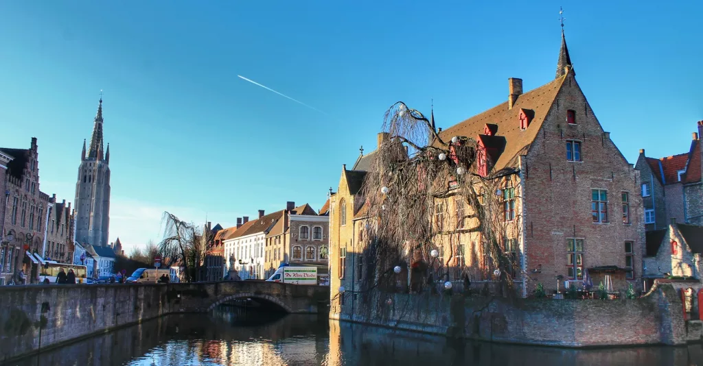 Rozenhoedkaai en Brujas con casas medievales reflejadas en el agua y una iglesia al fondo.