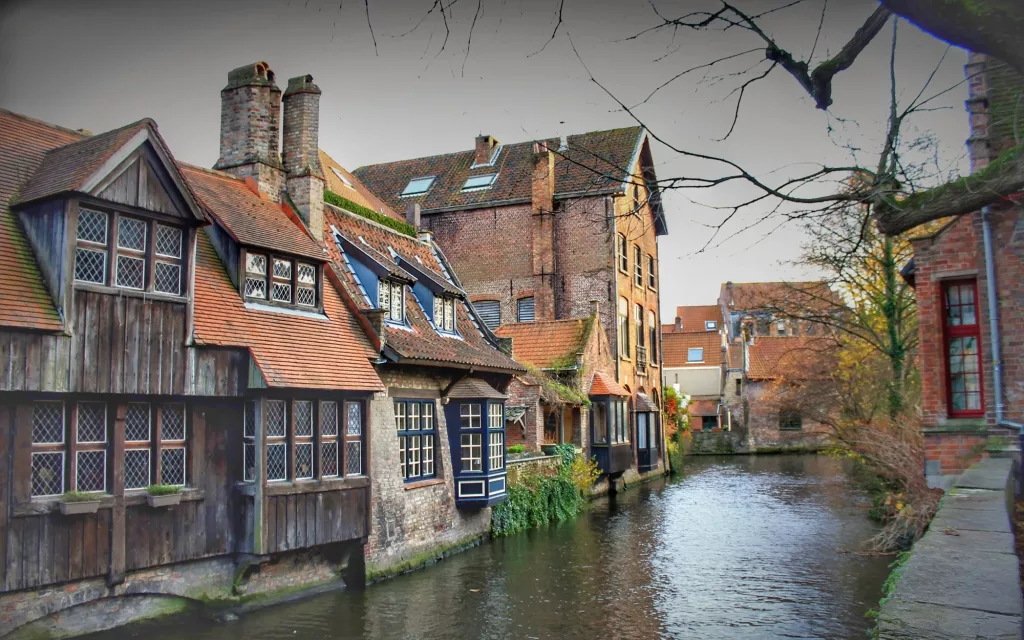 Casas de madera y ladrillo junto a un canal en Brujas, reflejadas en el agua.