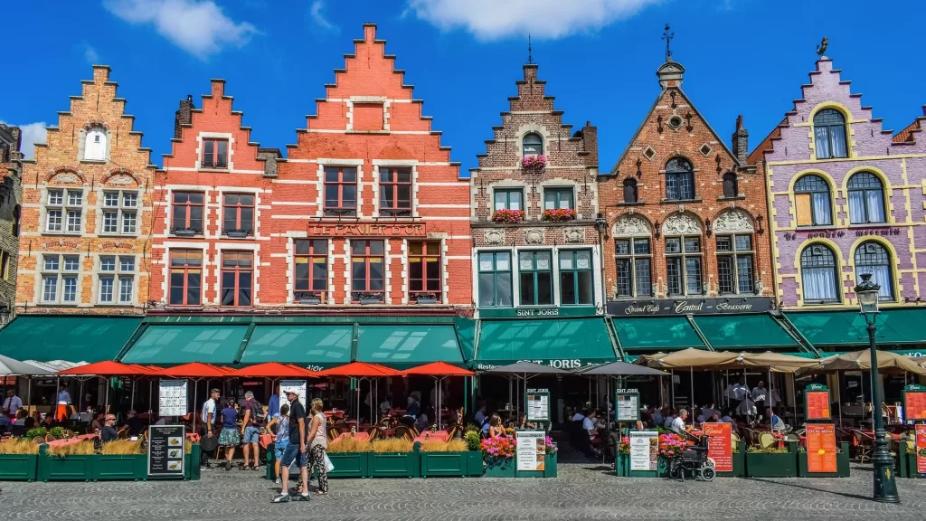 Fachadas coloridas en la Plaza Markt de Brujas con terrazas y turistas.