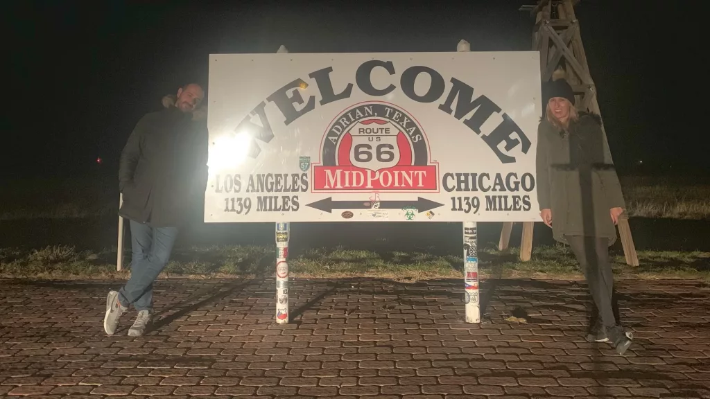 Ana y Miguelito de Two on Trip en el cartel del Midpoint en la Ruta 66 en Adrian, Texas.