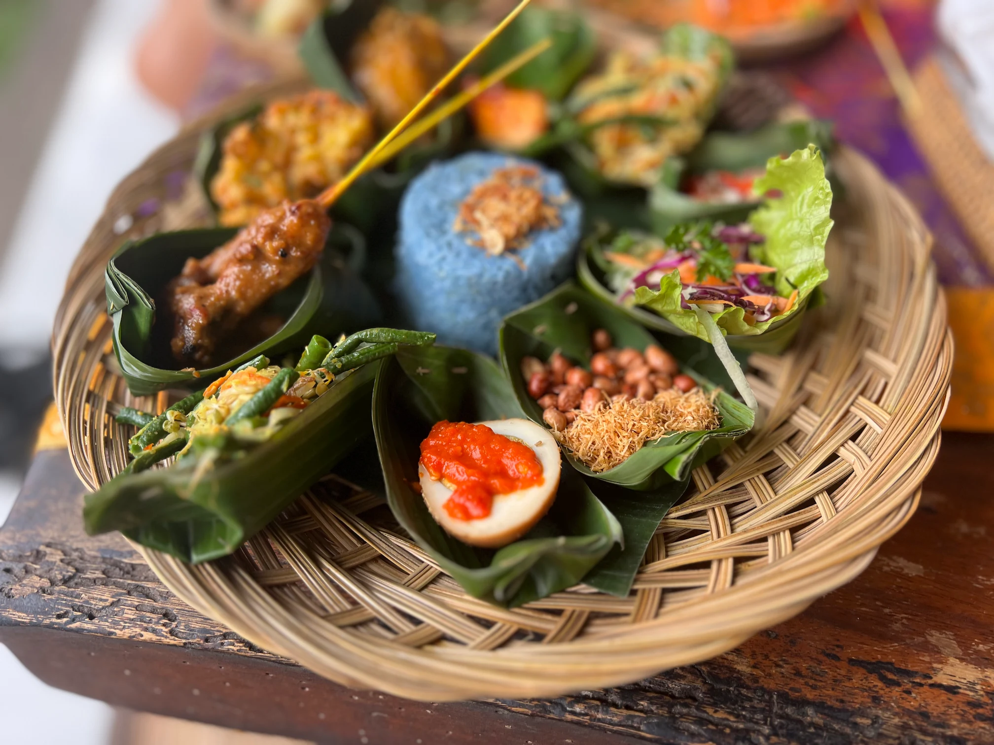 Platos típicos de Bali servidos en hoja de plátano, con arroz azul, satay y ensaladas.