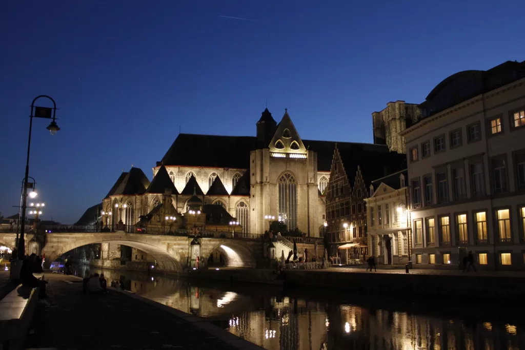 Vista nocturna de Gante con sus edificios iluminados reflejados en el río.