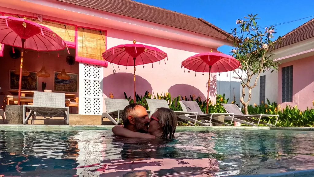 Pareja en la piscina del Hotel PinkPrivate Balangan, rodeados de decoración rosa y sombrillas balinesas.