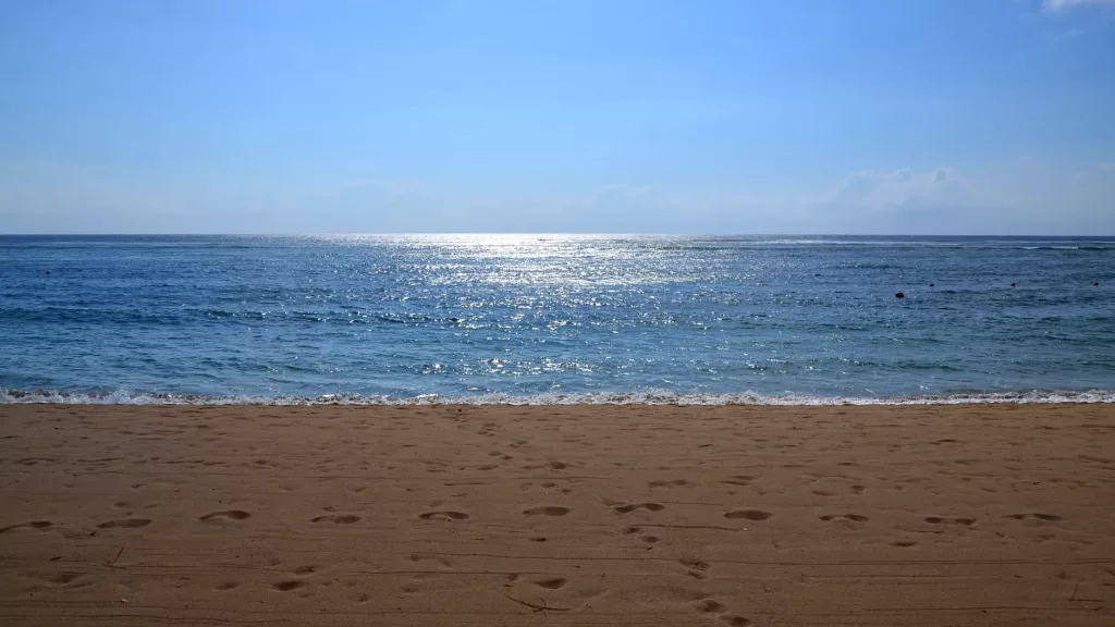 Vista del mar desde la playa de Kuta, con el sol reflejándose en el agua.