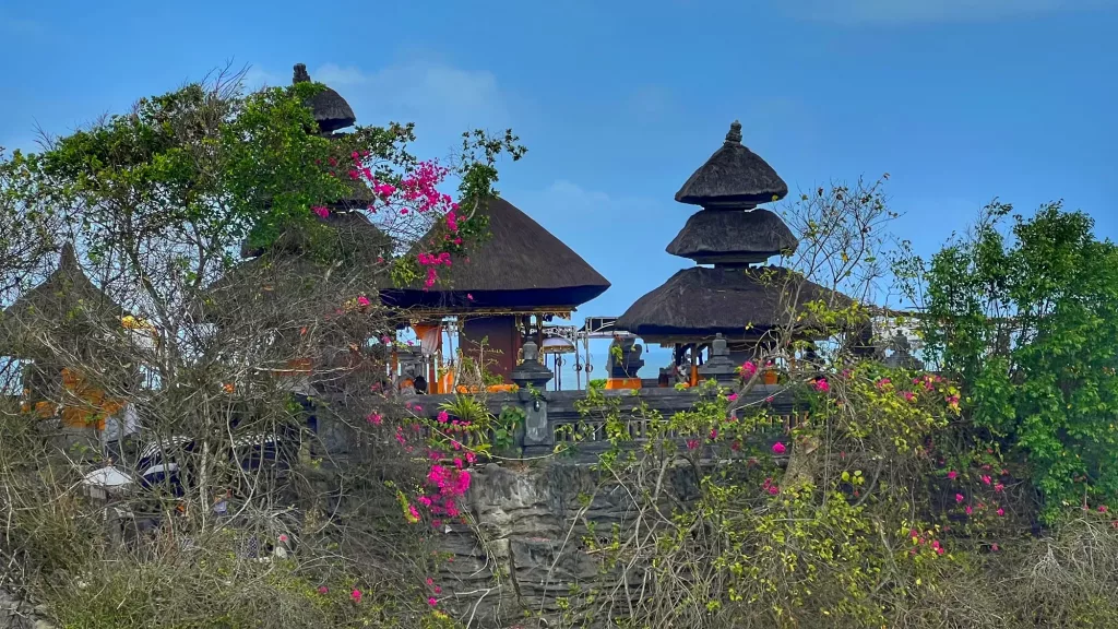 Templo balinés en un acantilado, rodeado de naturaleza y flores.
